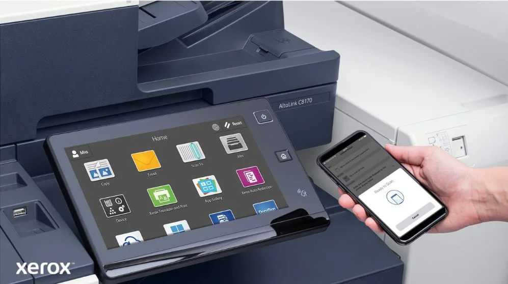 Gros plan de la main d'une personne tenant un smartphone, qui est connecté sans fil au panneau de commande à écran tactile d'une imprimante multifonction Xerox, mettant en valeur les capacités d'impression et de numérisation mobiles transparentes de Xerox
