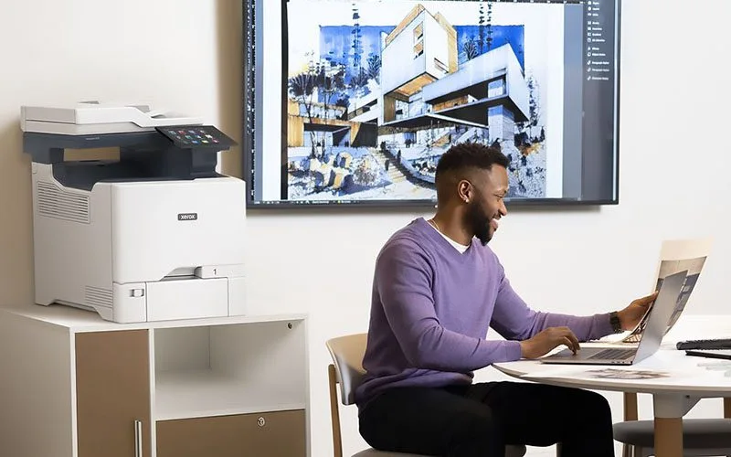 Hommes travaillant sur un ordinateur portable devant une Imprimante couleur multifonctions Xerox® VersaLink® C415