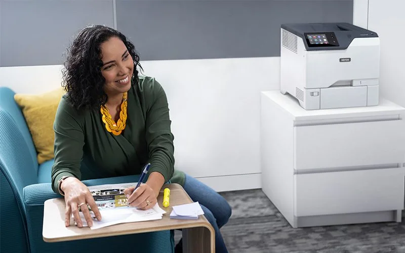 Femme souriante dans un bureau à côté de l'imprimante couleur Xerox® VersaLink® C620