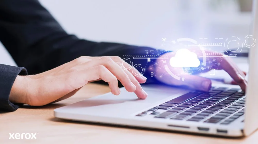 Les mains d'une personne sont représentées en train de taper sur un clavier d'ordinateur portable, avec une icône de nuage lumineux et des connexions réseau superposées sur l'image, symbolisant la connectivité cloud et les flux de travail numériques.