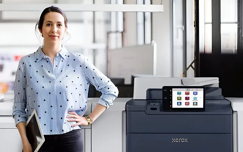 Une femme se tenant à côté de l'imprimante Xerox® PrimeLink® Série C9200 dans un environnement de bureau moderne