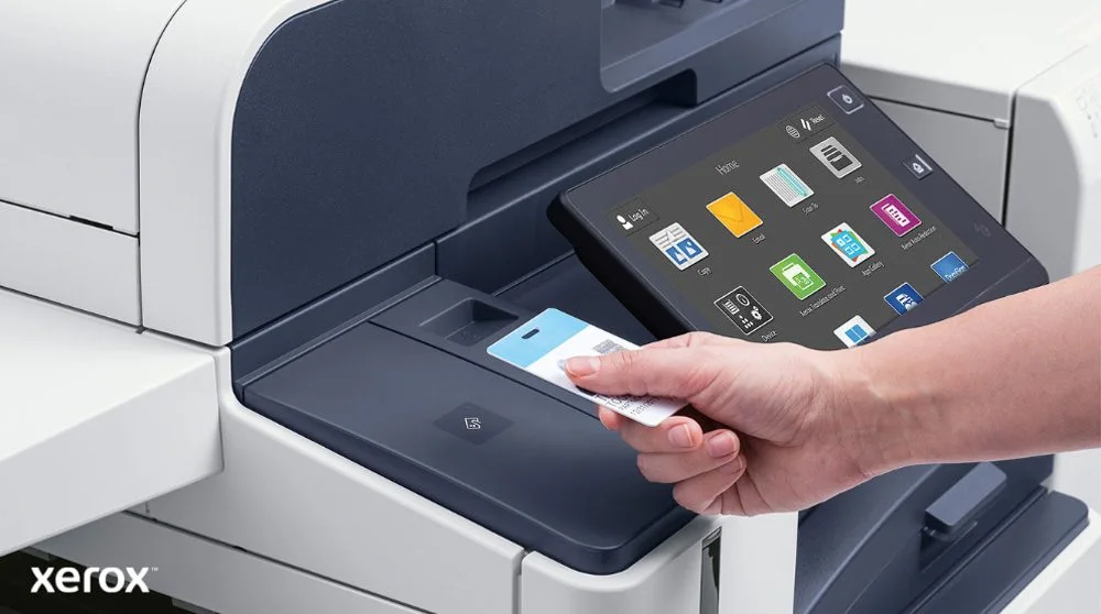 Une main tient une carte de sécurité et la scanne près du lecteur de carte d'une imprimante multifonction Xerox moderne dotée d'un grand écran tactile affichant diverses icônes d'application.